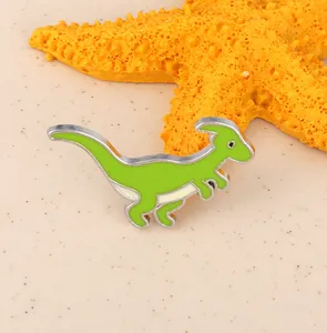 Close-up of green dinosaur enamel brooch pin next to a starfish on a textured background