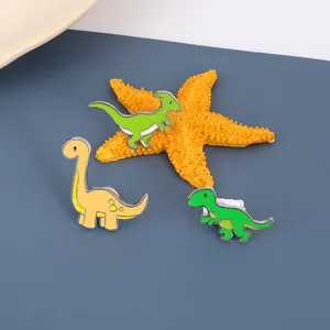 Detailed view of three cute enamel dinosaur brooches in green and yellow on blue background