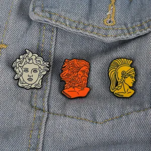 Drei Emaille-Pins mit griechischen Mythen wie Medusa und Prometheus auf Jeansjacke