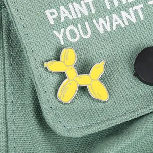 Primer plano de un pin esmaltado de perro globo amarillo en un bolso de lona verde oliva