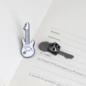 Close-up of a white electric guitar enamel brooch with a butterfly clasp on a notebook