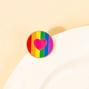 Close-up of a rainbow enamel pin with a pink heart on a sleek golden alloy background