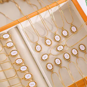 Macro view of oval gold plated pendants with white enamel and uppercase alphabet letters