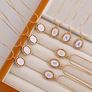 Macro detail of oval gold-plated titanium initial necklaces on cream velvet display