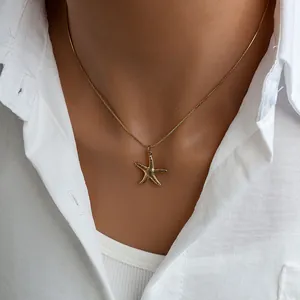 Detail view of a gold starfish pendant on a fine snake chain worn on a model's collarbone