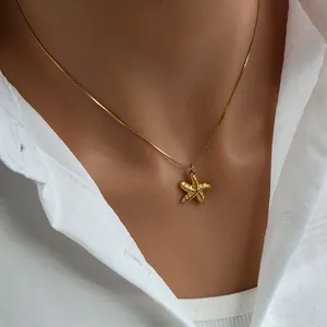 Detail of a gold starfish pendant necklace with embossed texture on a snake chain worn on neck