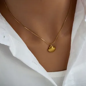 Detail of a minimalist gold shell pendant necklace on a model showing the snake chain texture