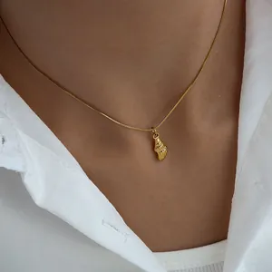 Close-up of a minimalist gold seashell pendant necklace worn on a white shirt