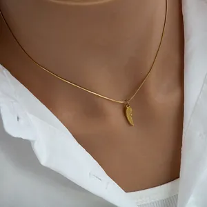 Detail of gold wing pendant and sleek snake chain on a white collar shirt