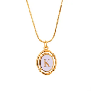 Detailed macro of gold oval pendant featuring letter K on a dainty snake chain necklace