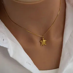 Detail shot of a turtle pendant necklace in gold finish worn with a white shirt