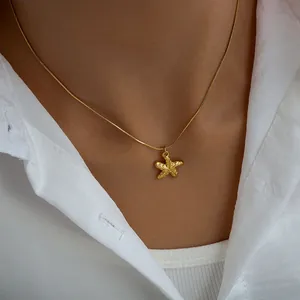 Detailed view of a gold-plated starfish pendant on a snake chain worn with a white shirt