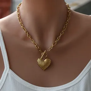 Detail of a gold heart pendant with radial texture and chunky chain with OT clasp toggle