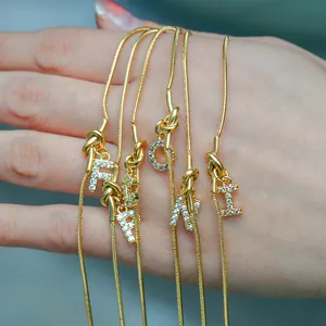 Detail van 18k vergulde slangenarmbanden met knoopontwerp en kristallen letters