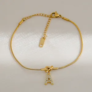 Detail van 18k vergulde knooparmband met een met zirkoon ingelegde A-letter hanger