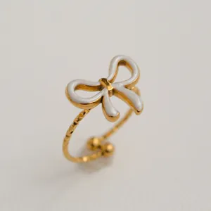 Détail de bague dorée ajustable avec nœud en nacre blanche et texture ondulée élégante