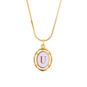 Close-up of gold snake chain necklace with an oval letter U pendant and purple disc