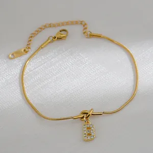 Detail van de gouden slangenarmband met knoop en zirkonia pavé letter B bedel hanger