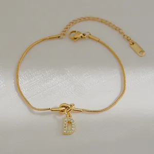 Detail van gouden knoop slangenketting armband met sprankelende zirkoon letter D