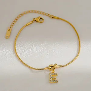 Detail van 18K vergulde slangenarmband met sprankelende hanger met de letter E