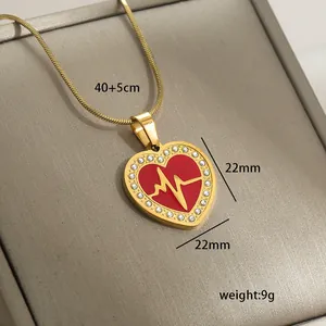 Detailed close-up of 14k gold heart pendant with red enamel and white crystal accents