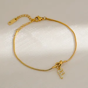 Detailopname van gouden letter F-hanger met zirkonia op een slangenketting armband