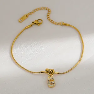 Detail van de gouden slangenschakelarmband met sprankelende letter G hanger en kristal