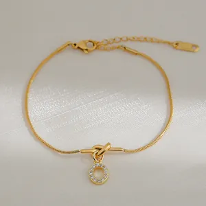 Detail van gouden slangenketting armband met zirkonia cirkel hanger en knoop design