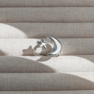 Vue macro d'une bague réglable étoile et croissant de lune argentée sur tissu beige