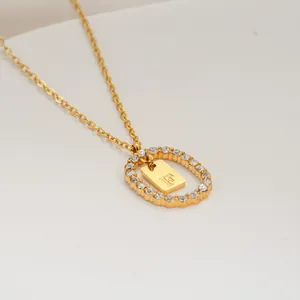 Macro del ciondolo ovale dorato con zirconi micro-incastonati e charm con lettera F