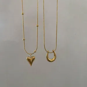 Details von goldenen Herz- und Hufeisen-Anhängern an minimalistischen Schlangenkettengliedern