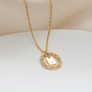 Dettaglio del pendente ovale dorato con zirconi brillanti e ciondolo con lettera V