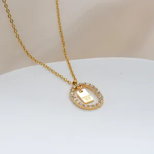 Dettaglio di un ciondolo ovale dorato con strass e lettera W incisa sul metallo