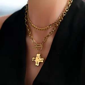 Detail of layered gold cuban and paperclip chains with hammered cross pendant and toggle clasp