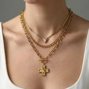 Three-layer gold necklace set with cross pendant and T-clasp on minimalist grey background