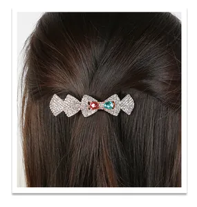 Detail of crystal bow hair clip with red and green gems on dark brown hair