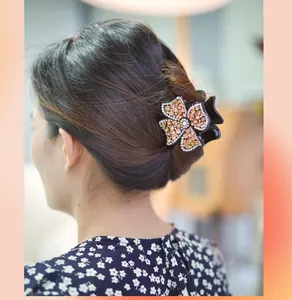 Detailed view of a four-leaf flower hair claw with orange rhinestones on an updo hairstyle