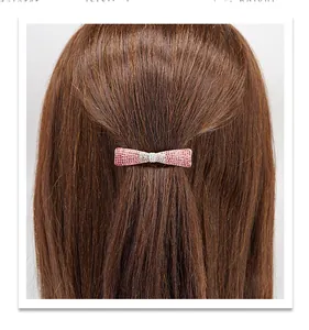 Detalle de un pequeño clip de lazo con pedrería rosa y azul en el cabello de una modelo