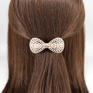 Elegant white pearl bow hair clip with rhinestones and gold base on brunette hair