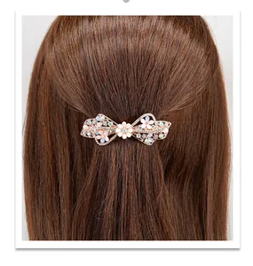 Detail van een bloemige strik haarklem met roze strass op lang bruin haar