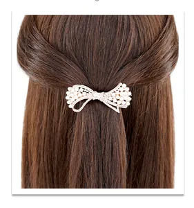 Détail d'une barrette noeud doré élégante avec perles blanches et cristaux sur cheveux bruns