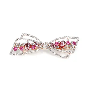 Barrette nœud dorée ornée de cristaux roses et strass blancs sur fond blanc épuré
