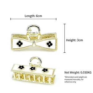Golden alloy bow-shaped hair claw with white enamel and black floral motifs, 6cm size