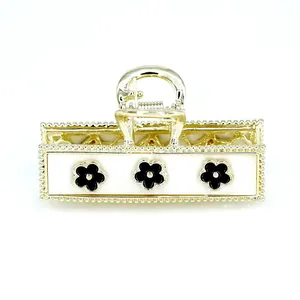 Elegant gold metal hair claw with white panel and black floral motifs on white background