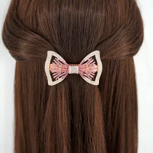 Pince à cheveux nœud en or rose ornée de strass roses et blancs sur cheveux bruns
