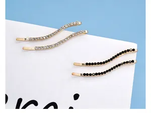 Dettaglio di fermagli per capelli a onde con strass bianchi e neri e base dorata