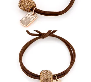 Détail d'un élastique marron avec une perle sertie de cristaux et une médaille dorée