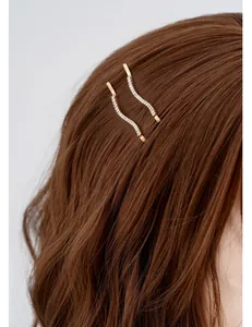 Dettaglio di forcine ondulate dorate con strass bianchi su capelli scuri ondulati