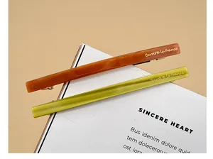 Détail des barrettes à ressort en acétate ambre et vert olive avec lettrage doré élégant