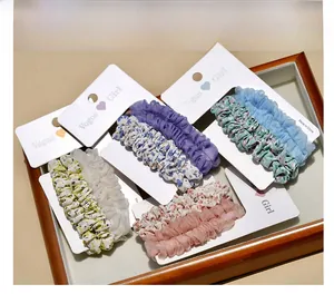 Detailed set of floral and chiffon scrunchies on white cards in a wooden tray